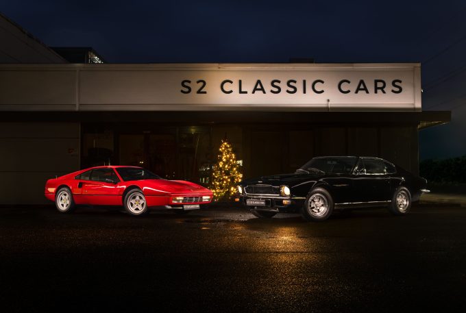 Ferrari 328GTb en Aston Martin AMV8 met een kerstboom in het midden. het is donker dus de lampen van de kerstboom en rondom de auto's zijn mooi verlicht